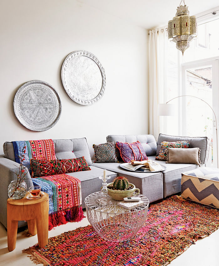 Oriental atmosphere with colourful fabrics, grey sofa set, metal trays on wall and typical Moroccan pendant lamps